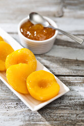Bowl of peach jam and plate with halves of peaches on wooden table - MAEF008039