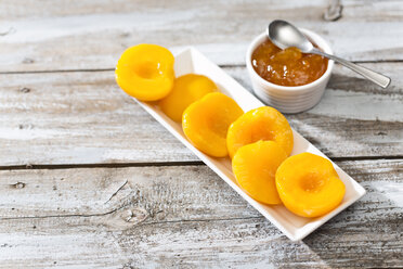 Bowl of peach jam and plate with halves of peaches on wooden table - MAEF008040