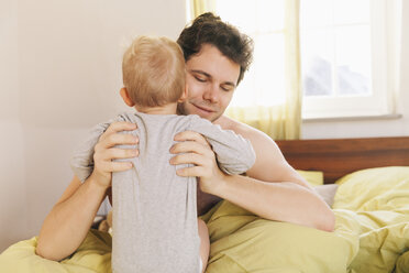 Father sitting in bed, lifting up toddler - MFF000908