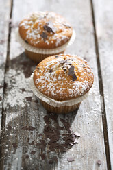 Zwei Muffins in Papierförmchen mit Puderzucker bestreut auf Holztisch - MAEF008046