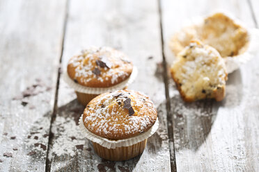 Zwei Muffins in Pappbechern und ein halber Muffin im Hintergrund auf einem Holztisch - MAEF008050