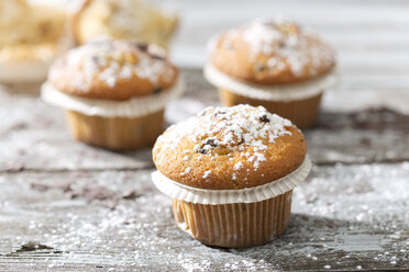 Muffins in Papierförmchen mit Puderzucker bestreut auf Holztisch - MAEF008065