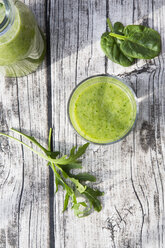 Glasflasche und Glas mit grünem Smoothie, bestehend aus Spinat, Rucola, Apfel, Orange, Banane und Gurke, auf grauem Holztisch, Blick von oben - LVF000762