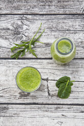 Glasflasche und Glas mit grünem Smoothie, bestehend aus Spinat, Rucola, Apfel, Orange, Banane und Gurke, auf grauem Holztisch, Blick von oben - LVF000760