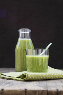 Glasflasche und Glas mit grünem Smoothie, bestehend aus Spinat, Rucola, Apfel, Orange, Banane und Gurke, auf Holztisch - LV000781