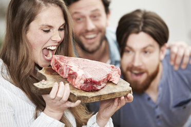 Happy young womanpretending to bite into raw steak - FMKF000998