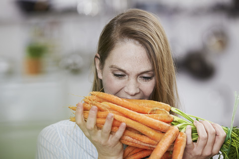 Junge Frau hält ein Bündel Karotten in der Küche, lizenzfreies Stockfoto