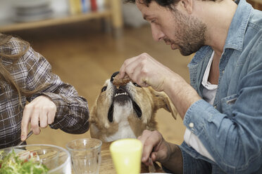 Mann isst am Tisch und füttert Hund - FMKF001101