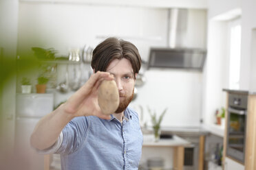 Mann in Küche hält Kartoffel - FMKF001042