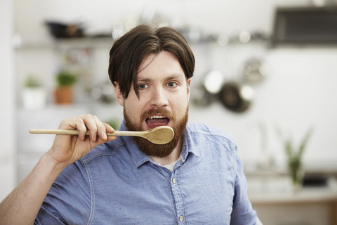 Man cooking in kitchen tasting from wooden spoon stock photo