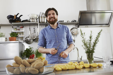 Smiling man preparing potatoes in kitchen - FMKF001059