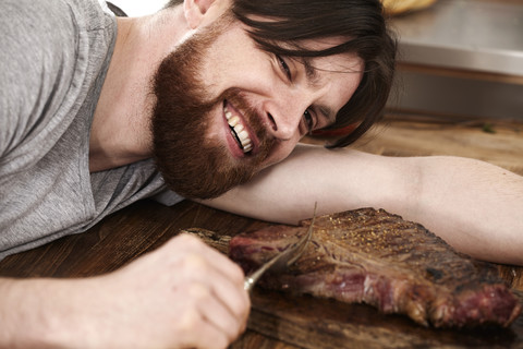 Happy man lying on table looking at large steak stock photo