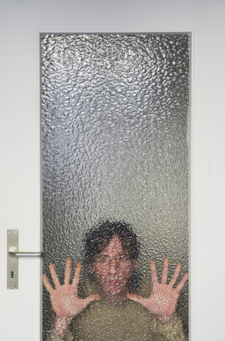 Mann schaut durch eine gerippte Glasscheibe einer Tür, lizenzfreies Stockfoto