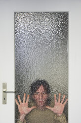 Mann schaut durch eine gerippte Glasscheibe einer Tür - MUF001456