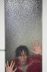 Man looking through ribbed glass pane of door - MUF001457