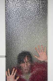 Mann schaut durch eine gerippte Glasscheibe einer Tür - MUF001457