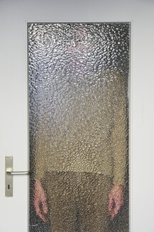 Man standing behind closed door with ribbed glass pane - MUF001453