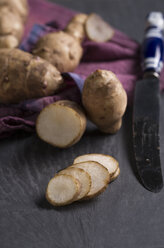 Sliced and whole sunroots (Helianthus tuberosus), knife and cloth on slate - MYF000206