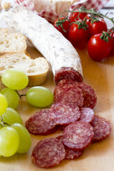 Gehackte Salami, grüne Weintrauben, Tomaten und Baguette auf dem Schneidebrett - SARF000292