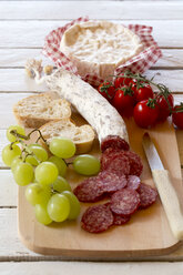 Gehackte Salami, grüne Weintrauben, Camembert, Tomaten und Baguette auf dem Schneidebrett - SARF000294