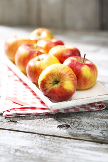 Schale mit acht Bio-Äpfeln auf Küchenhandtuch und Holztisch - MAEF008070