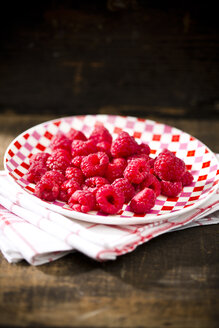 Schale mit Himbeeren auf Küchenhandtuch und Holztisch - MAEF008066