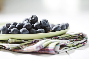 Dish of blueberries on kitchen towel and white wooden table - MAEF008077