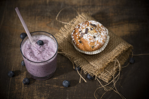 Glas Blaubeermilchshake, Blaubeermuffin und Blaubeeren auf Holztisch, Blick von oben - MAEF008092