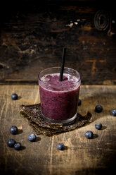 Glas Heidelbeer-Smoothie und Heidelbeeren auf Holztisch - MAEF008099