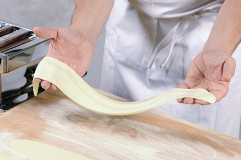 Die Hände eines Mannes halten den ausgerollten Nudelteig für hausgemachte Tortelloni, lizenzfreies Stockfoto