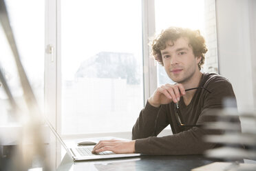 Portrait of young architect sitting at desktop in his office - FKF000422