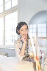 Portrait of young female architect thinking at her desktop in office - FKF000451