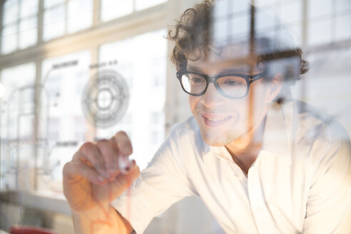 Porträt eines jungen Architekten, der einen Bauplan an einer Glasscheibe im Büro befestigt - FKF000456