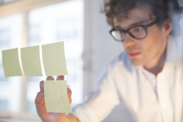 Porträt eines jungen Architekten, der Notizen an einer Glasscheibe im Büro befestigt - FKF000453