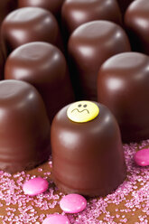 Chocolate marshmallows, one decorated with smiley face, pink sugar and chocolate drops in front - CSF020940