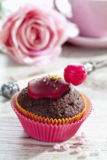 Schokoladenmuffin in Muffinpapier dekoriert mit rotem Lolly und Zuckerguss auf gedecktem Tisch - CSF020955