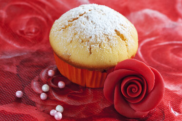 Muffin aus Muffinpapier, Marzipanblüte und Zuckerperlen auf rotem Blumenmuster - CSF020971