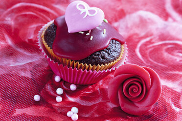Dekorierter Muffin aus Muffinpapier, Marzipanblüte und Zuckerperlen auf rotem Blumenmuster - CSF020972