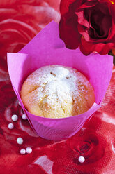 Muffin in rosa Verpackung, Rosenblüten und Zuckerperlen auf rotem Blumenmuster - CSF020974