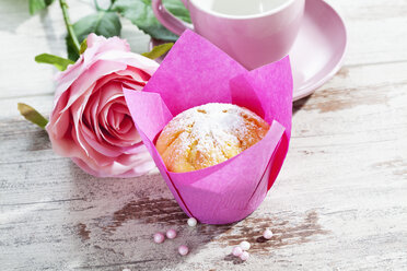 Muffin in rosa Verpackung, Rosenblüte, Tasse und Zuckerperlen auf Holztisch - CSF020975