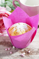 Muffin in rosa Verpackung, Rosenblüte, Tasse und Zuckerperlen auf Holztisch - CSF020976