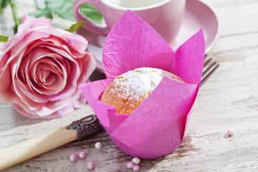 Muffin in rosa Verpackung, Rosenblüte, Tasse, Gabel und Zuckerperlen auf Holztisch - CSF020977