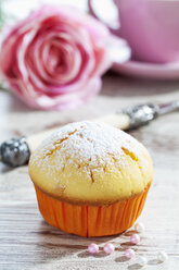 Muffin in Pappbecher, Rosenblüte, Tasse, Gabel und Zuckerperlen auf Holztisch - CSF021018