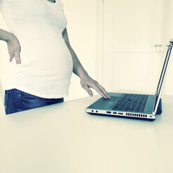 Schwangere Frau steht mit Laptop am Tisch, asiatisch, Freiburg, Deutschland - DRF000547
