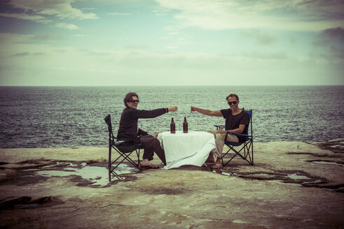 Australien, Sydney, zwei Männer sitzen mit Bier am Tisch auf einer Klippe - FBF000279