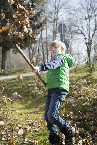 Junge mit Harke wirft Herbstlaub in die Luft, lizenzfreies Stockfoto