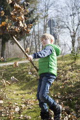 Junge mit Harke wirft Herbstlaub in die Luft - SARF000329