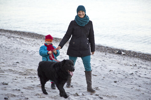 Deutschland, Schleswig-Holstein, Kiel, Mutter und Tochter gehen mit Labrador am Strand spazieren - JFEF000322