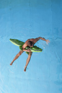 Junger Mann mit Badespielzeug im Wasser schwimmend, Blick von oben - PAF000550