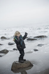 Germany, Mecklenburg-Western Pomerania, Ruegen, happy little boy standing on rock at waterside - MJF000954